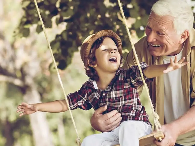 A grandfather pushing his grandson on a swing outdoors.